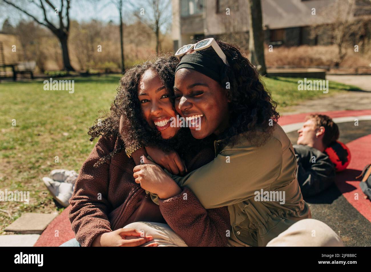 Happy multiracial female friends embracing each other while sitting in playground on sunny day Stock Photo