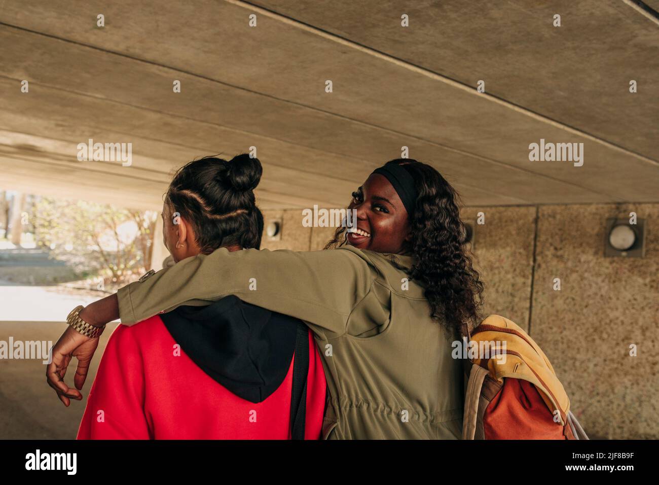 Portrait of smiling woman with arm around male friend walking together in underpass Stock Photo