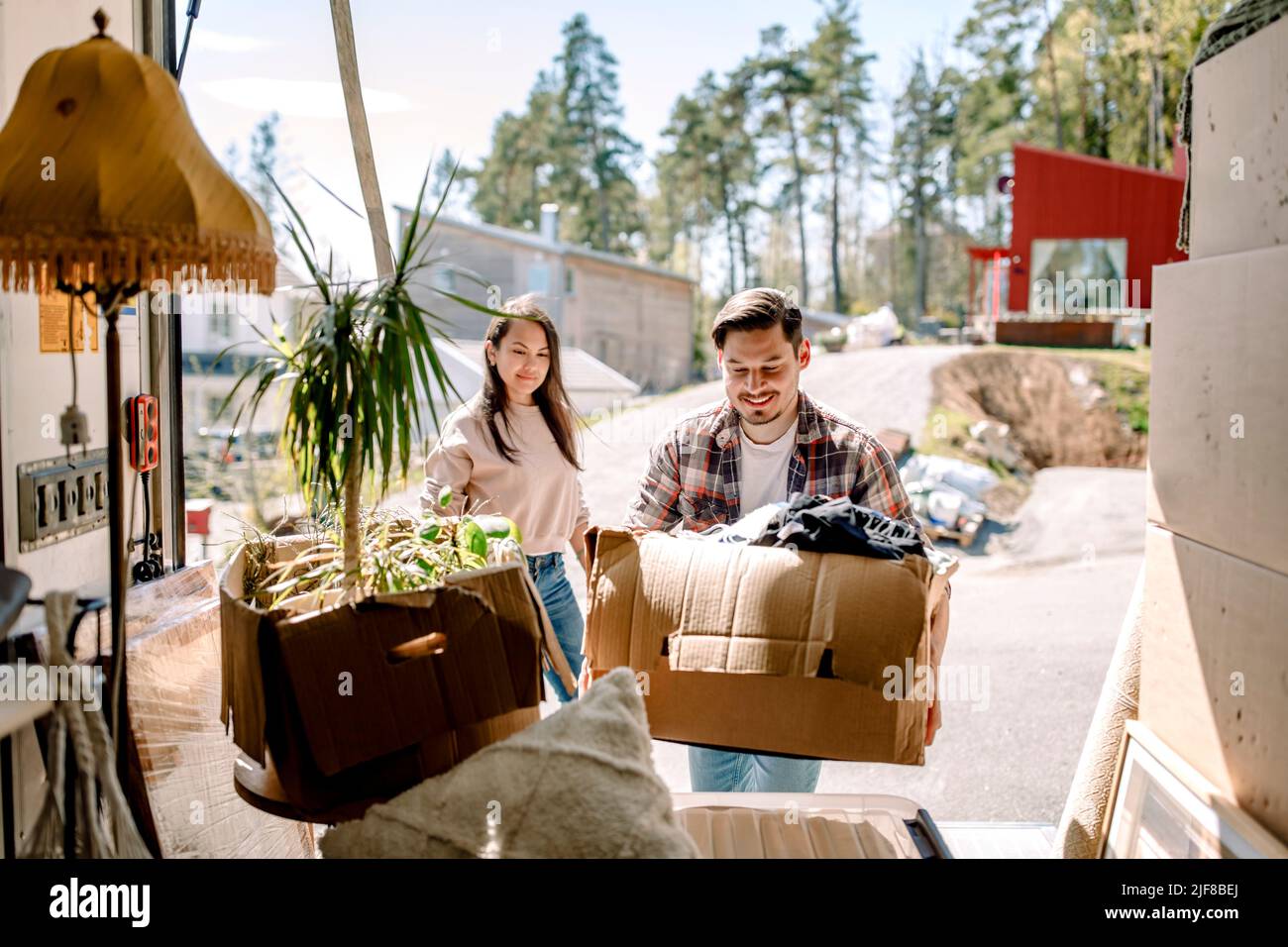 Couple picking cardboard boxes from delivery truck on sunny day Stock Photo