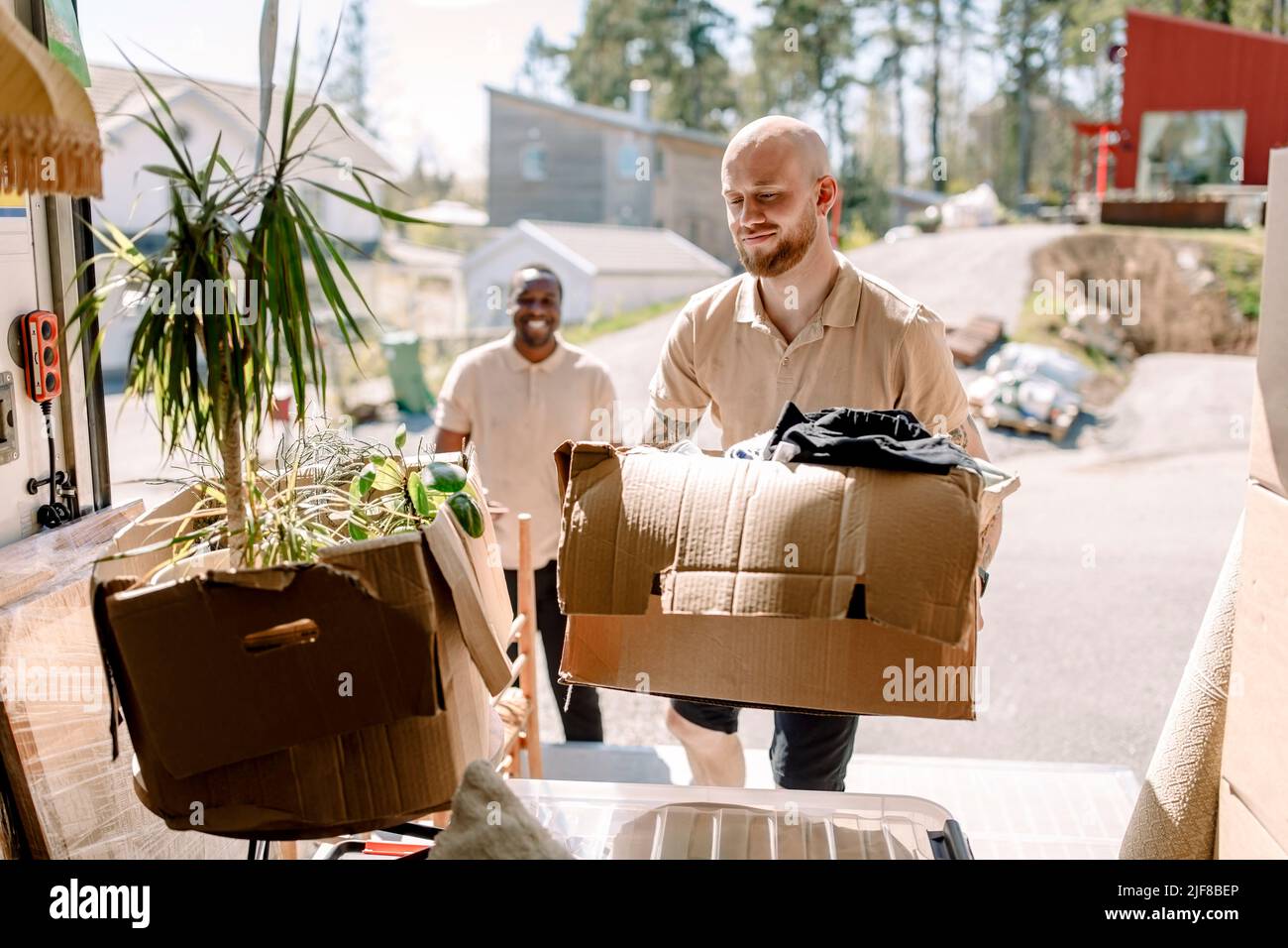 Multiracial movers carrying boxes from truck during sunny day Stock Photo