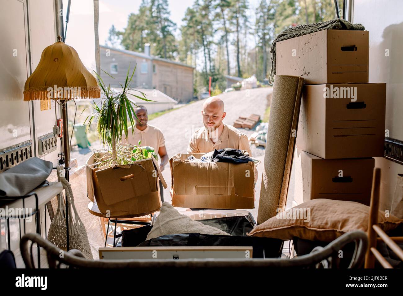 Multiracial movers unloading cardboard boxes from truck Stock Photo
