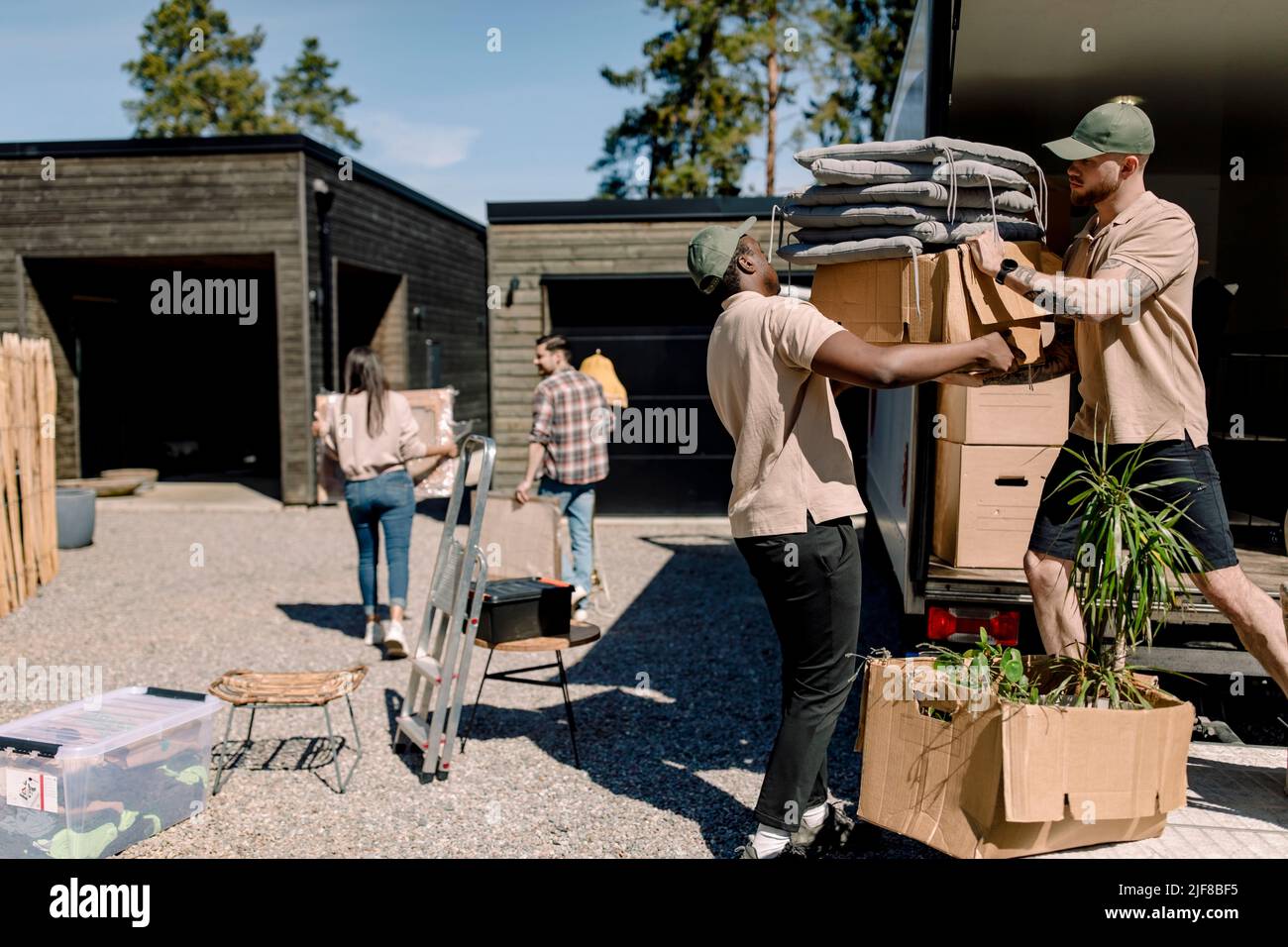 Multiracial movers unloading boxes from truck while couple in background Stock Photo