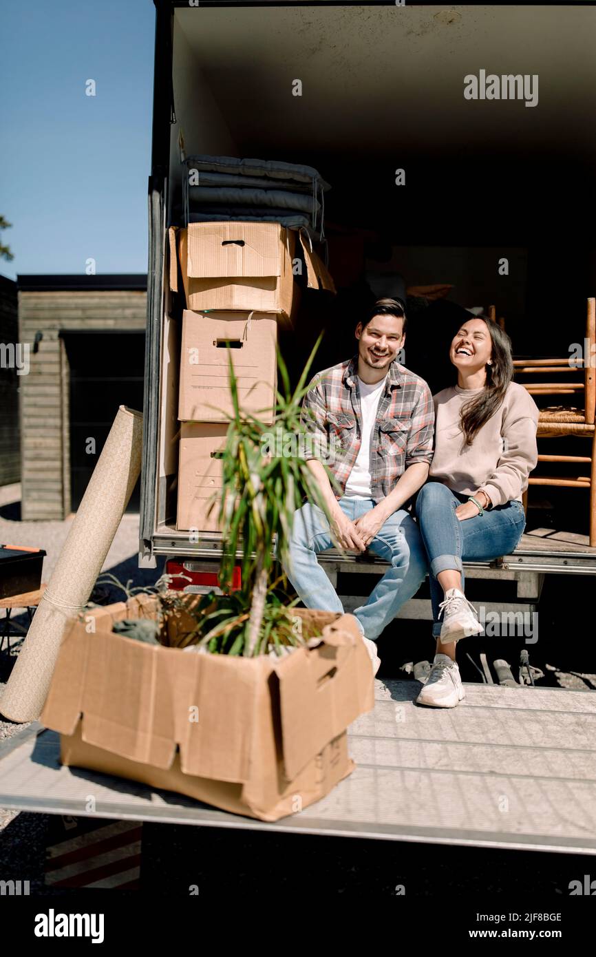 Portrait of happy couple sitting in delivery truck during sunny day Stock Photo