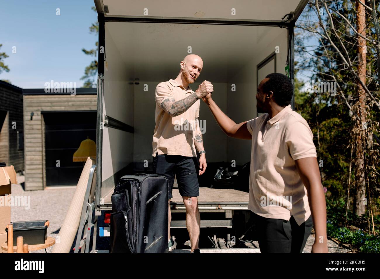 Multiracial delivery company employees shaking hands while standing outside truck Stock Photo