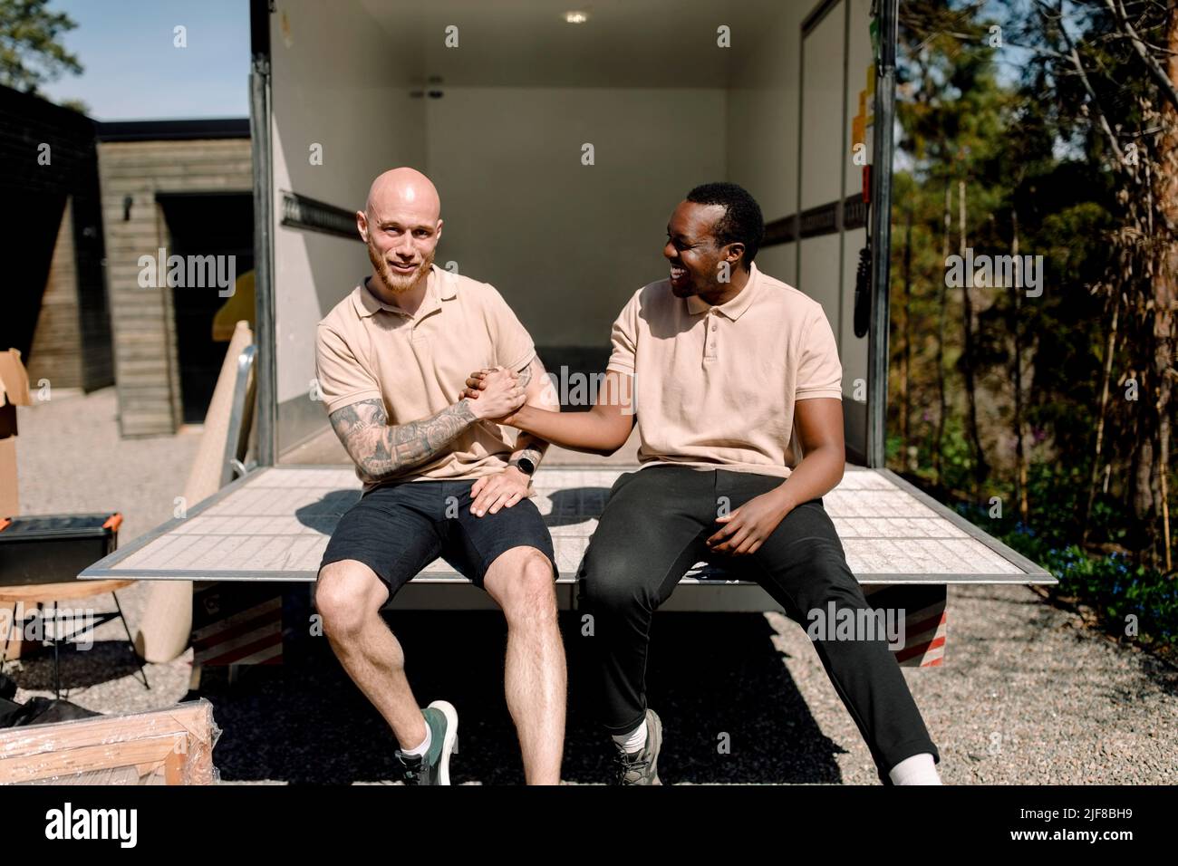 Smiling multiracial delivery men shaking hands while sitting in truck during sunny day Stock Photo