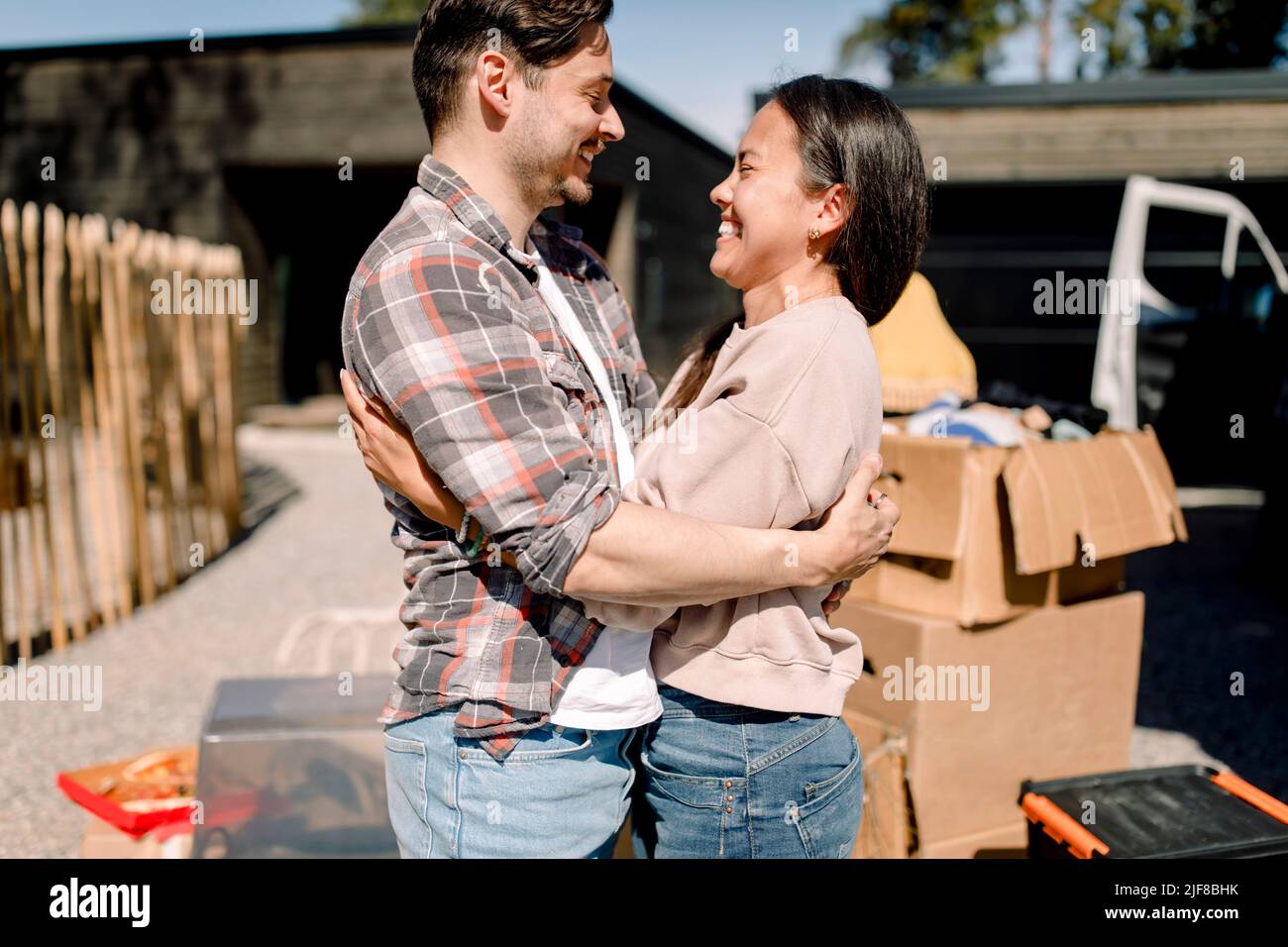 Happy couple embracing while standing outside new house during sunny day Stock Photo