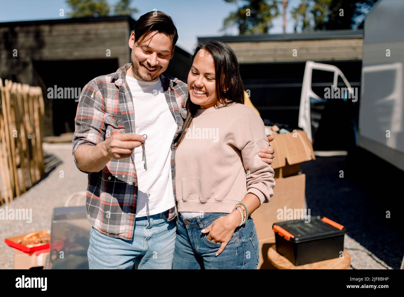 Smiling couple looking at key of new house while standing outside new house Stock Photo