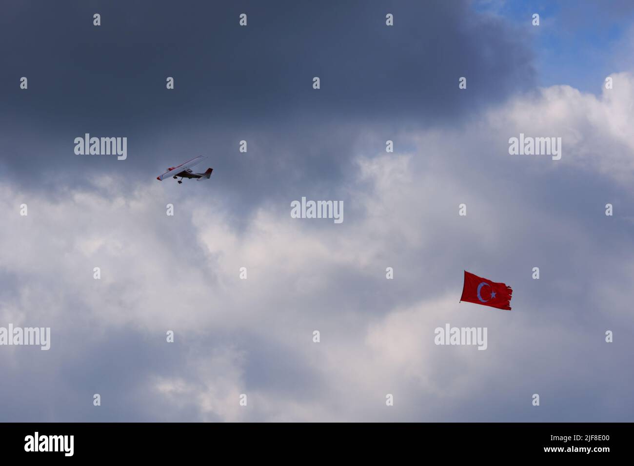 Model plane towing Turkish flag in airshow flying within dark clouds Stock Photo