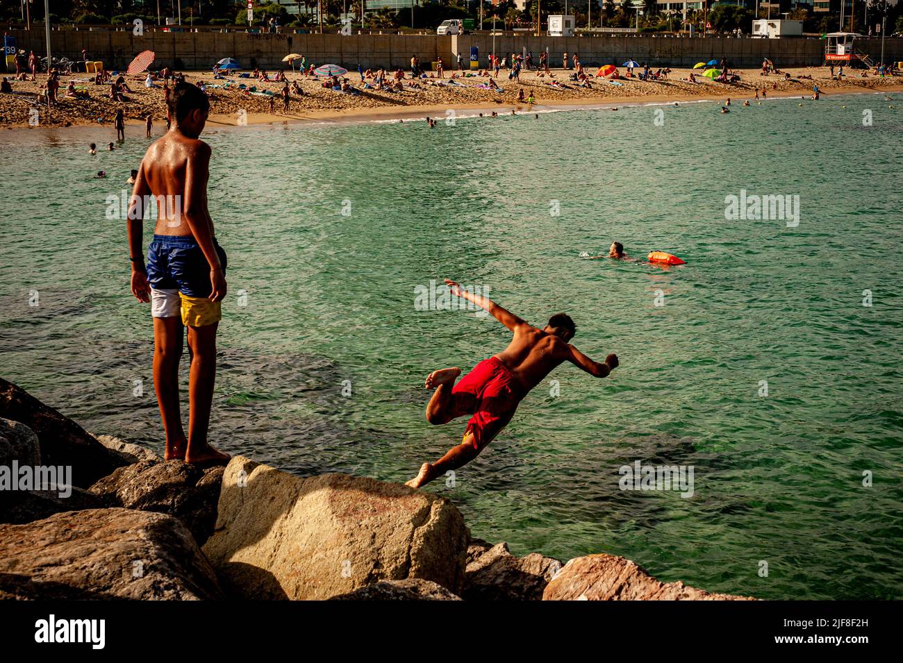 Young boy jumps to the sea from a breakwater at Llevant beach in Barcelona. Barcelona City Council has published a report warning that it is necessary to monitor whether carcinogenic substances are emerging in an area of Llevant beach. The City Council has had the results since last February but has not released them so far as required by various environmental organizations. Stock Photo