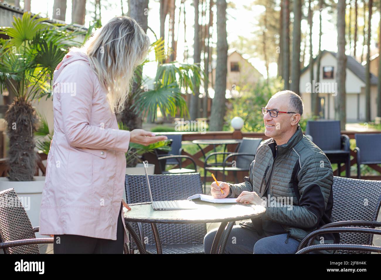 Portrait of smiling middle-aged man father writing down notes in notepad, listening to young woman daughter in cafe. Stock Photo