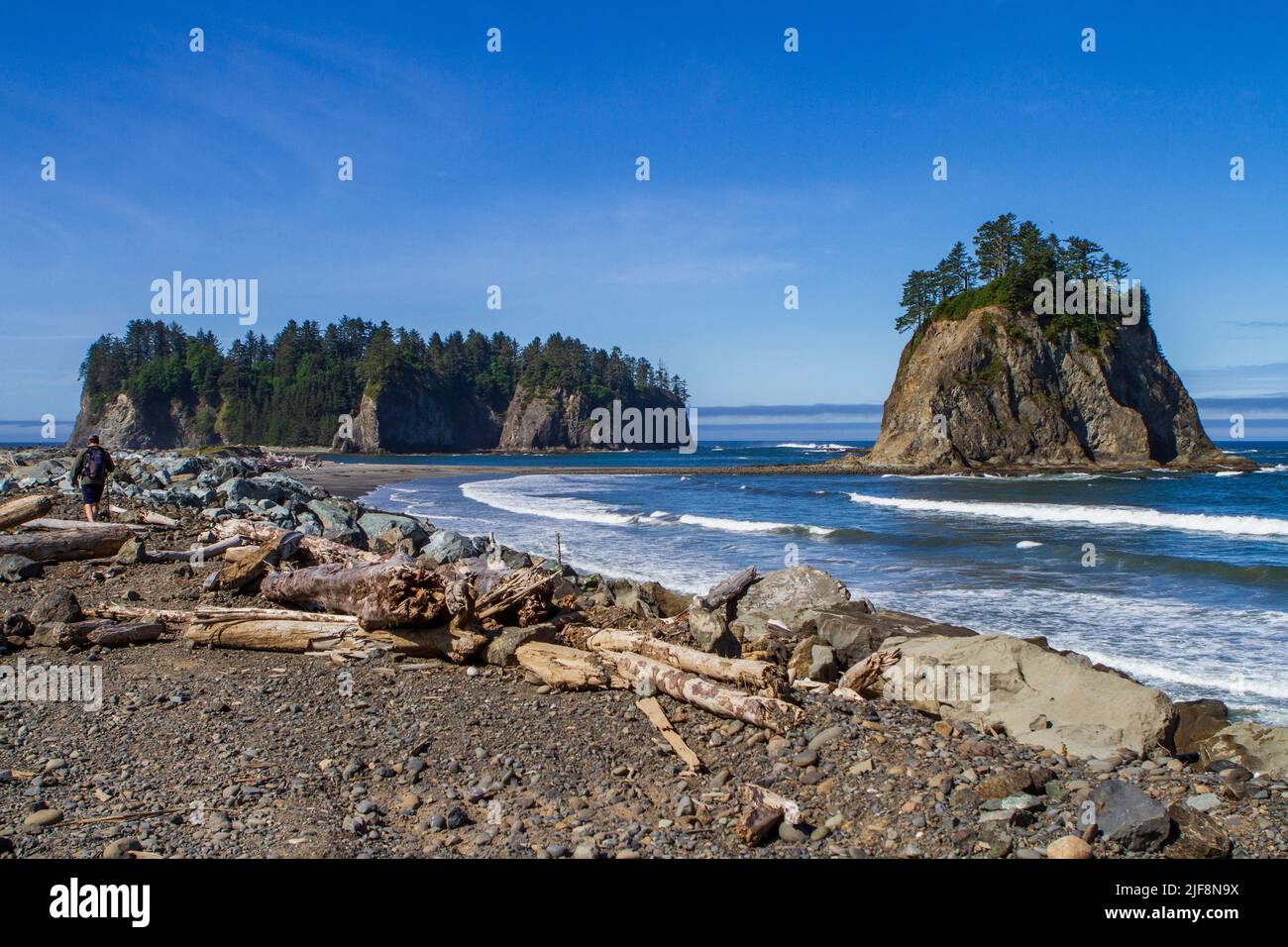 A man with a daypack walks along the spit toward James and Little James Islands, part of the Quileute tribal lands near Rialto Beach, Washington, USA. Stock Photo