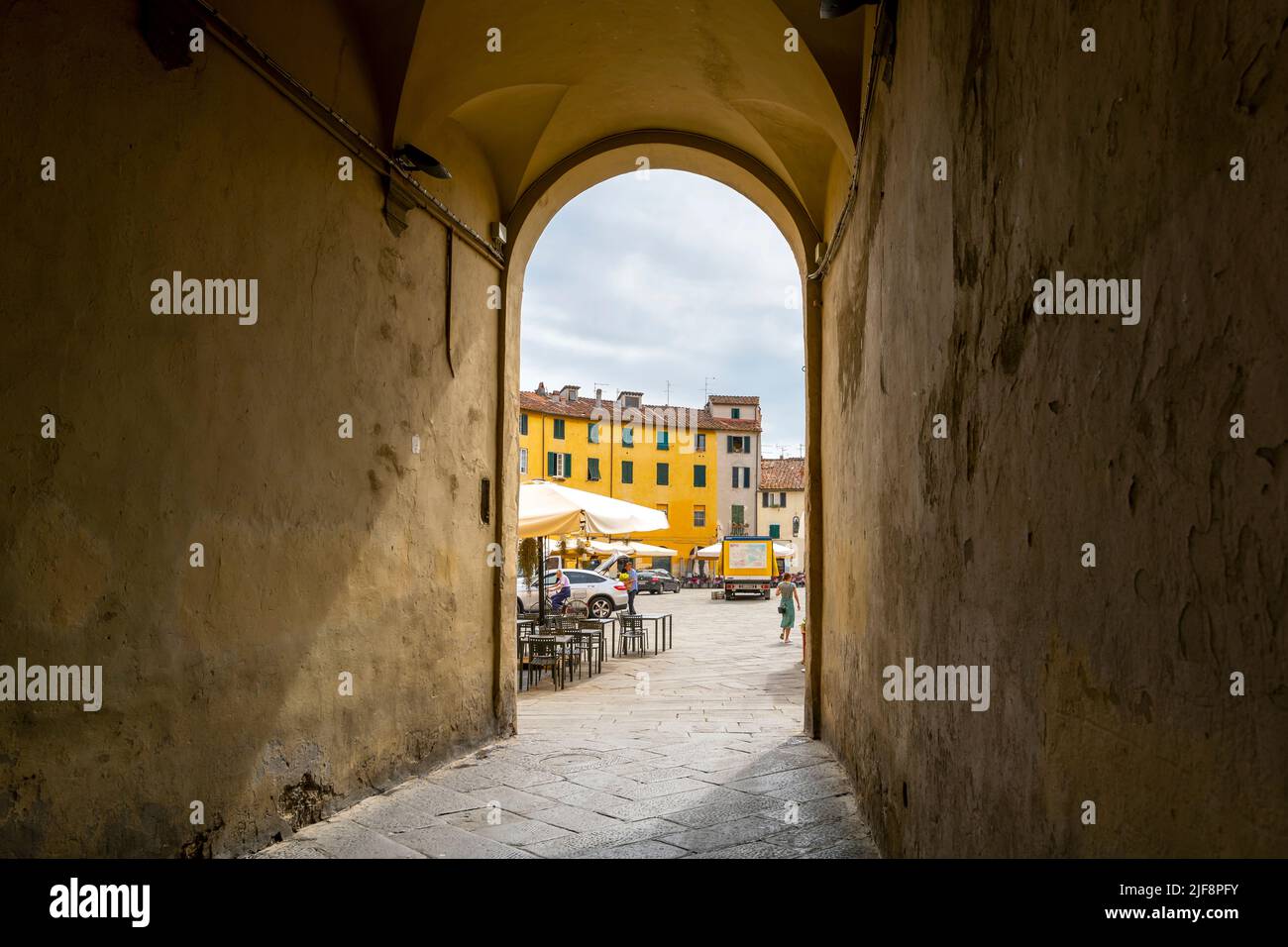 An arched tunneled entry into the ancient amphitheater, now Piazza del Anfiteatro in Lucca Italy, with cafes and shops. Stock Photo