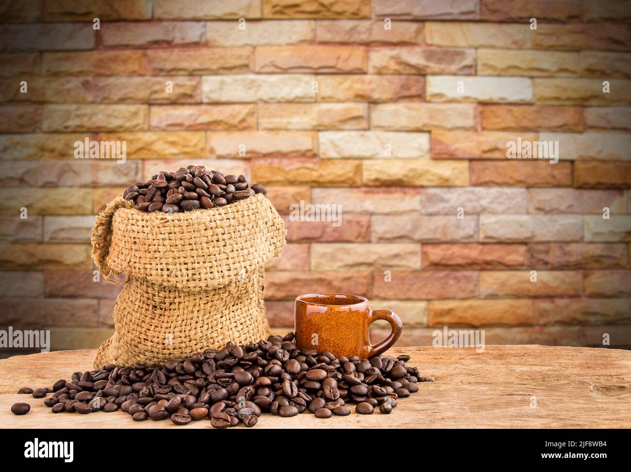 Coffee beans in burlap sack on wooden table with blurred brick wall background Stock Photo