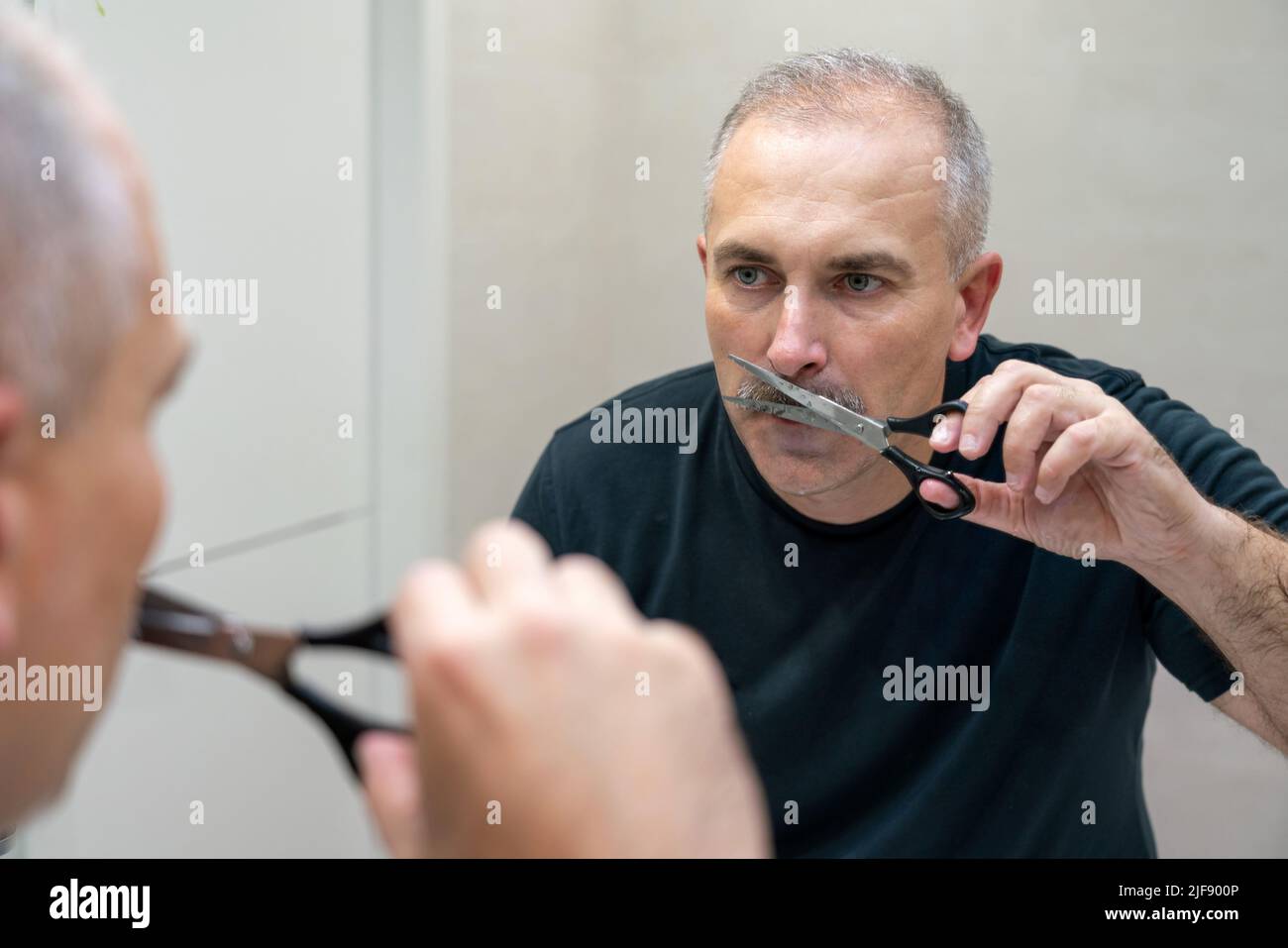 Middleaged handsome man using scissors to cut his mustache Stock Photo