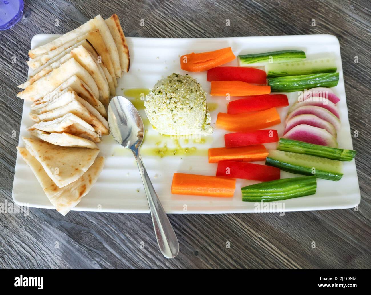 Edamame hummus with pita bread triangles, carrot sticks, cucumbers, and radishes on white serving platter. Stock Photo