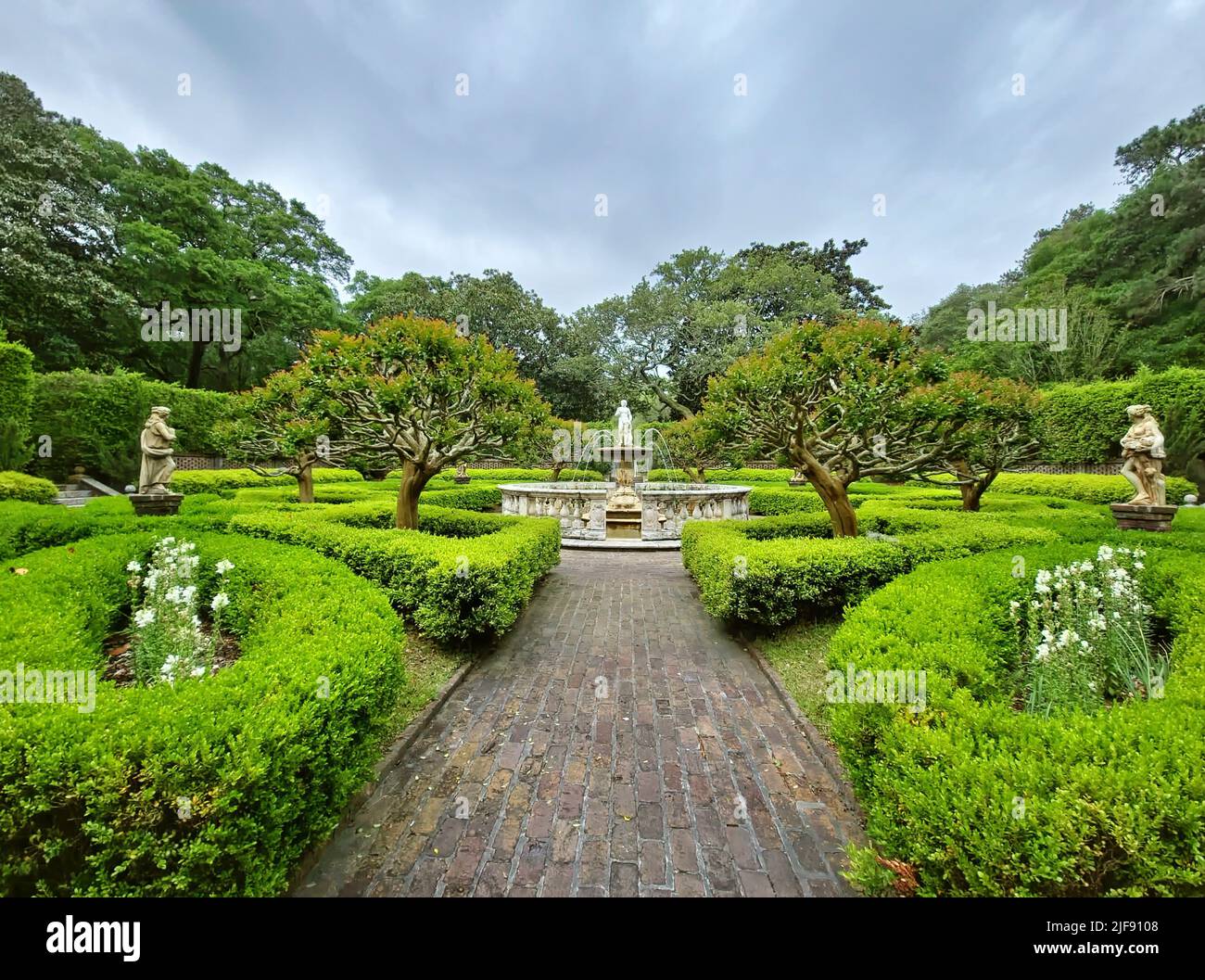 Formal garden with statues, fountain, brick walkway, and manicured