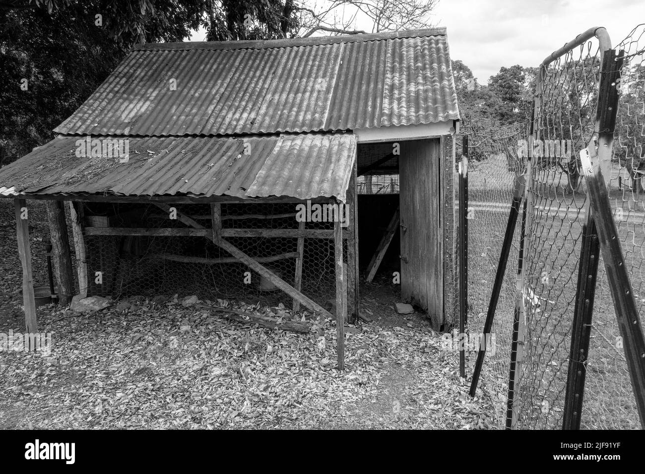 An old dilapidated rusting chicken house fenced with netted wire, empty and no longer in use Stock Photo