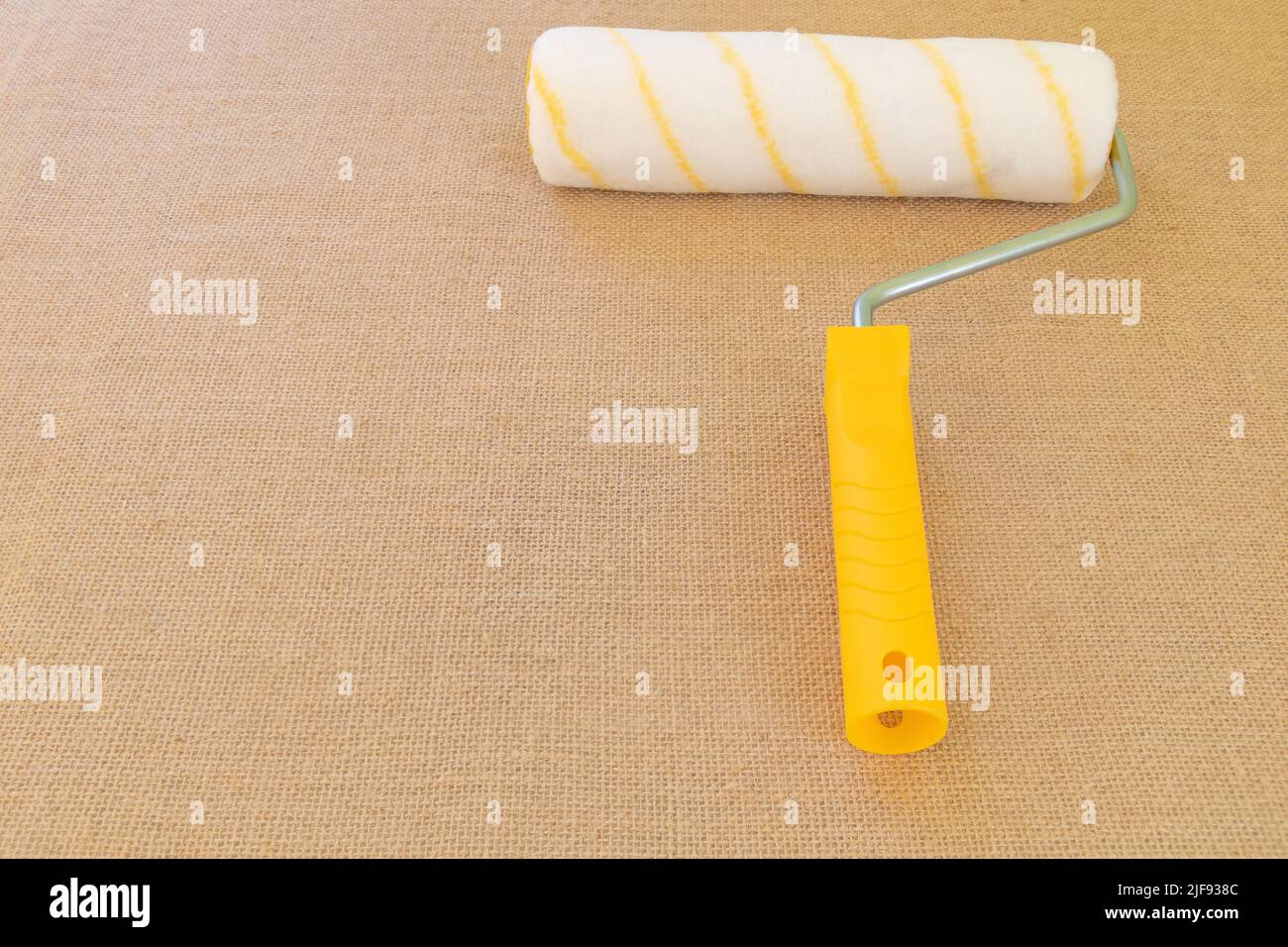 A roller with a yellow handle on a rustic fabric background Stock Photo