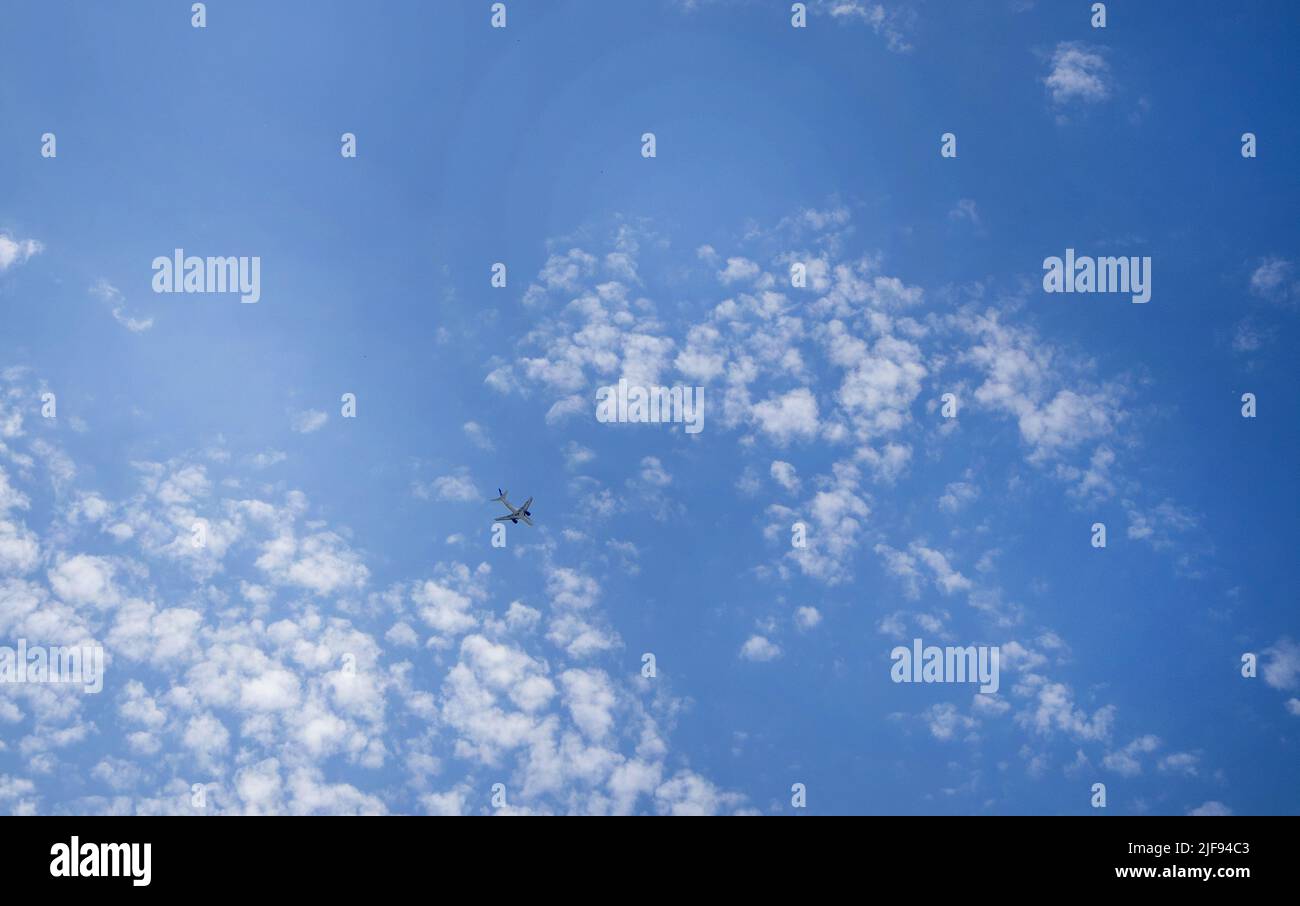 The plane is flying in a blue sky among clouds and sunlight, a copy of space. Stock Photo