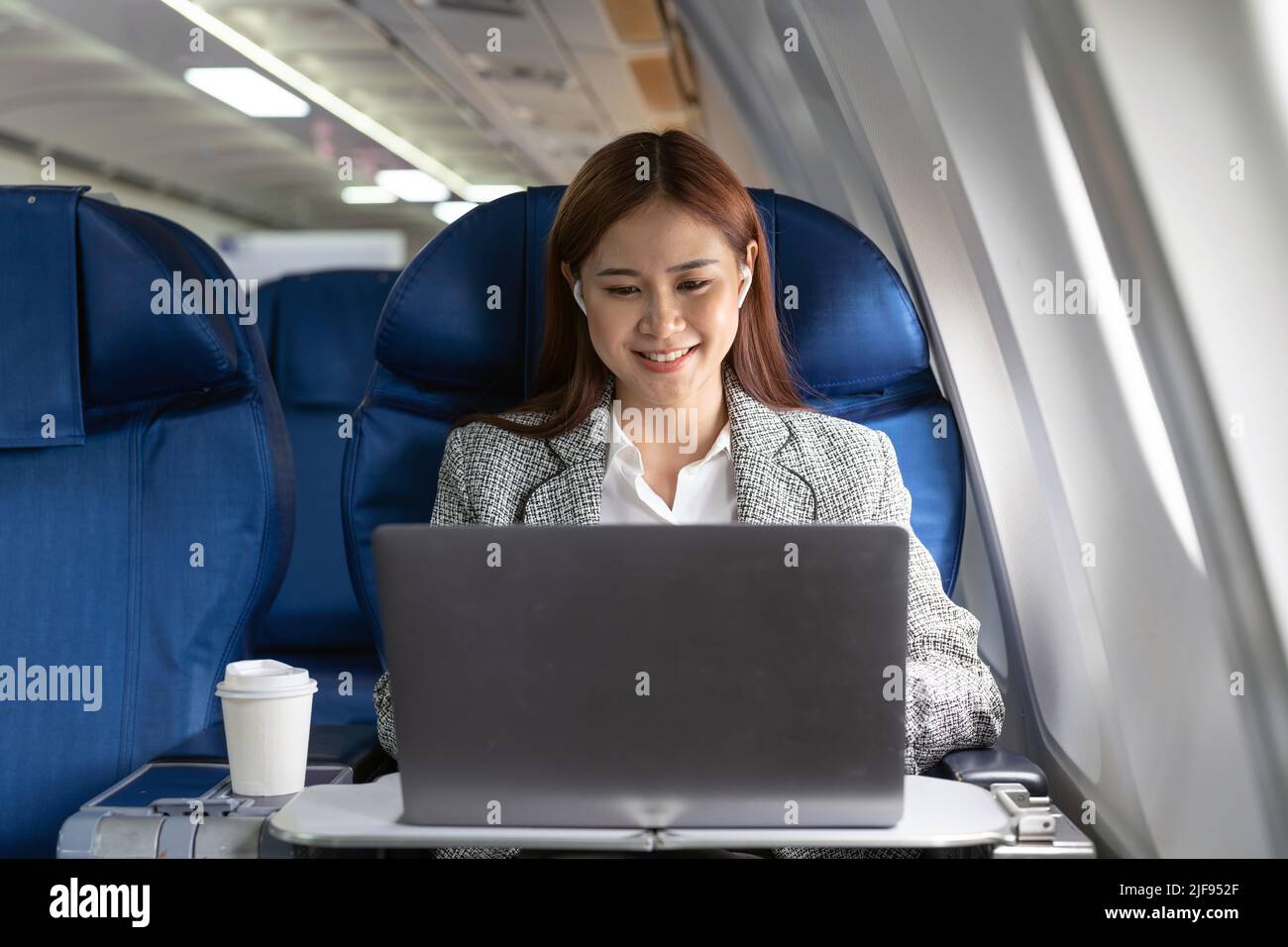 Traveling and technology. Flying at first class. Pretty young asian businees woman working on laptop computer while sitting in airplane Stock Photo
