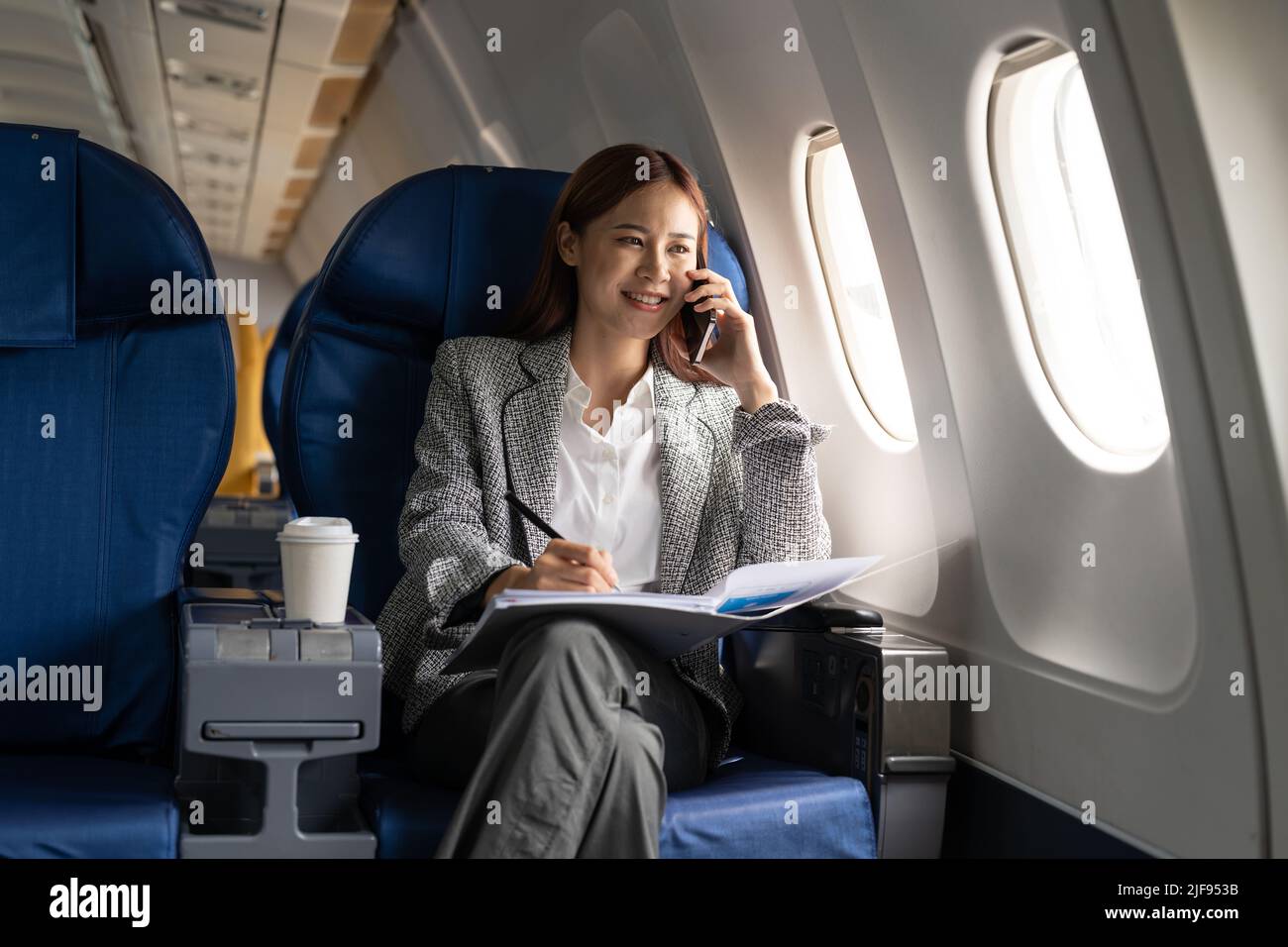 Young attractive and successful business asian woman talking on the phone and working while sitting in the chair of his private business plane Stock Photo