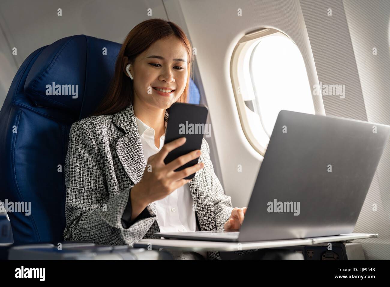 Happy and cheerful asian businesswoman using smartphone and laptop computer during flight. Urban lifestyle Stock Photo