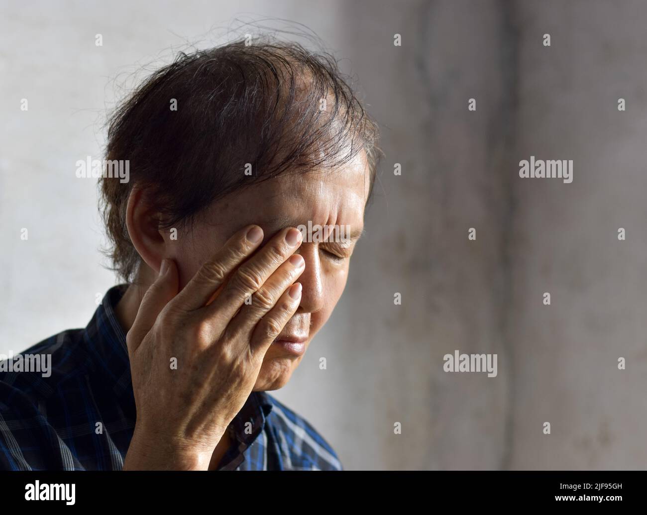 Asian elder man rubbing his eye. Concept of eye strain or itchy eyelid. Stock Photo