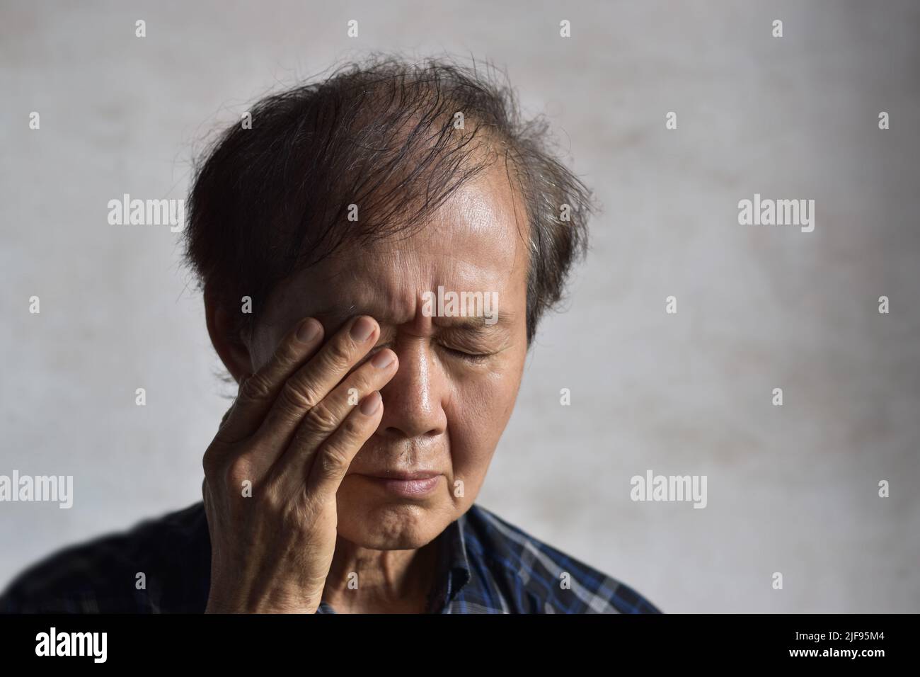 Asian elder man rubbing his eye. Concept of eye strain or itchy eyelid. Stock Photo