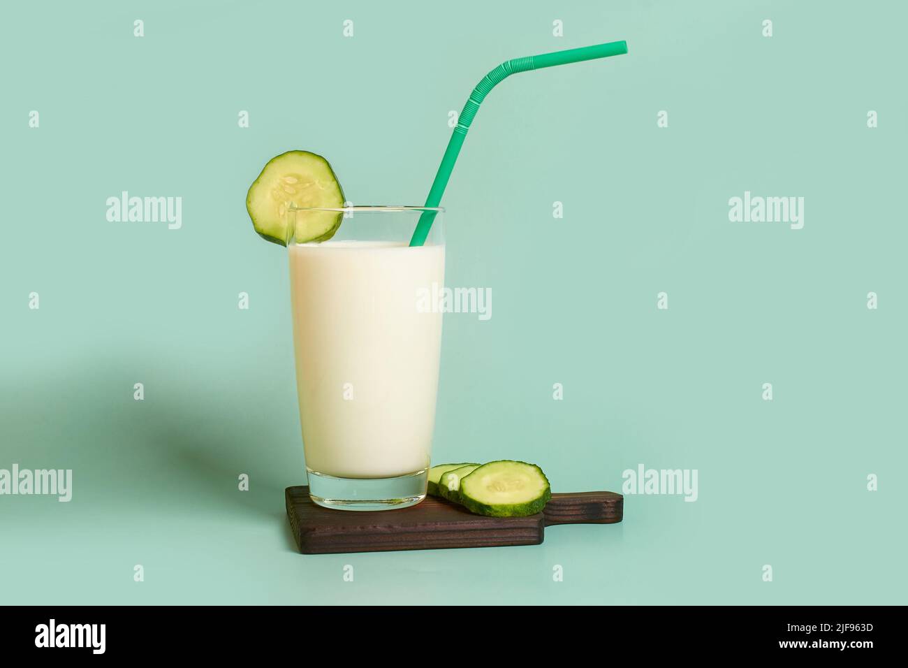 Glass with milk, plastic tube and cucumber slices on a wooden stand  Stock Photo