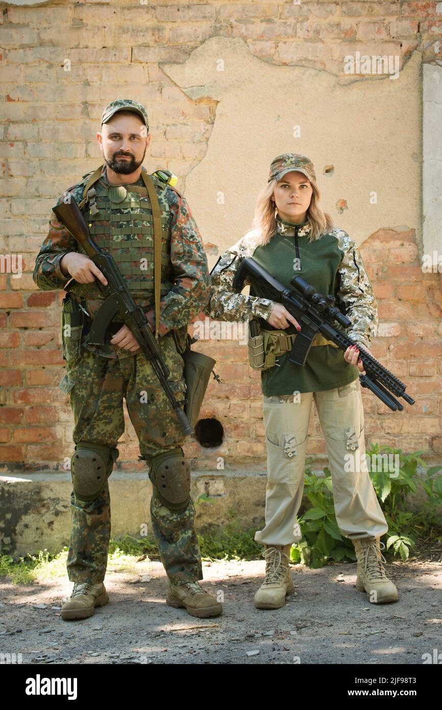 Man and woman, Ukrainian defenders with weapons near the destroyed building during the war in Ukraine Stock Photo