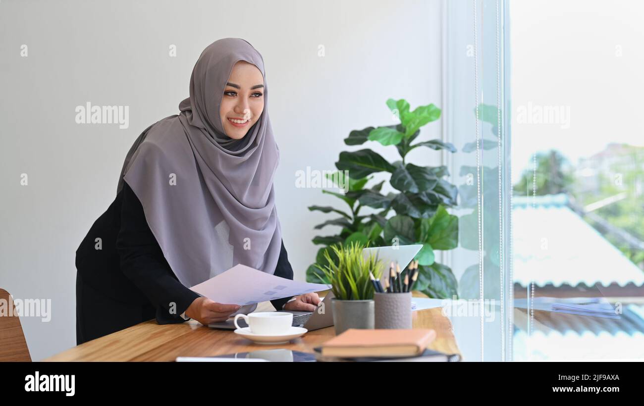 Beautiful young Muslim business woman in hijab standing in modern ...