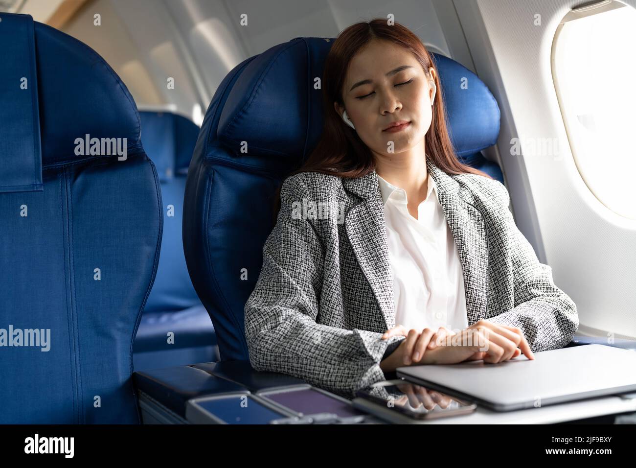 Tired business asian lady napping on seat while traveling by airplane. Commercial transportation by planes. Stock Photo