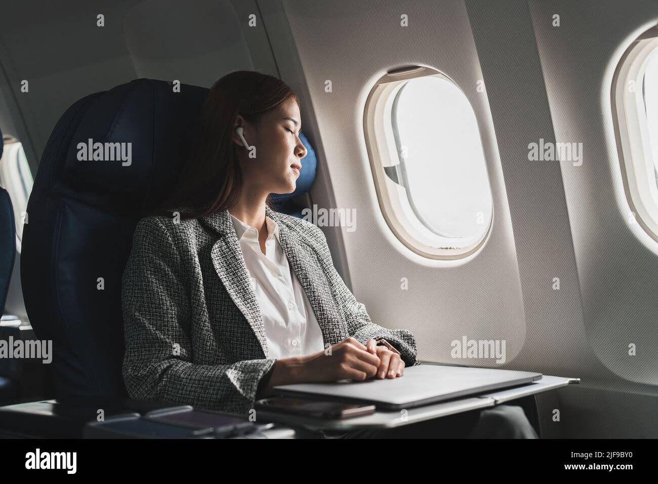 Tired business asian lady napping on seat while traveling by airplane. Commercial transportation by planes. Stock Photo