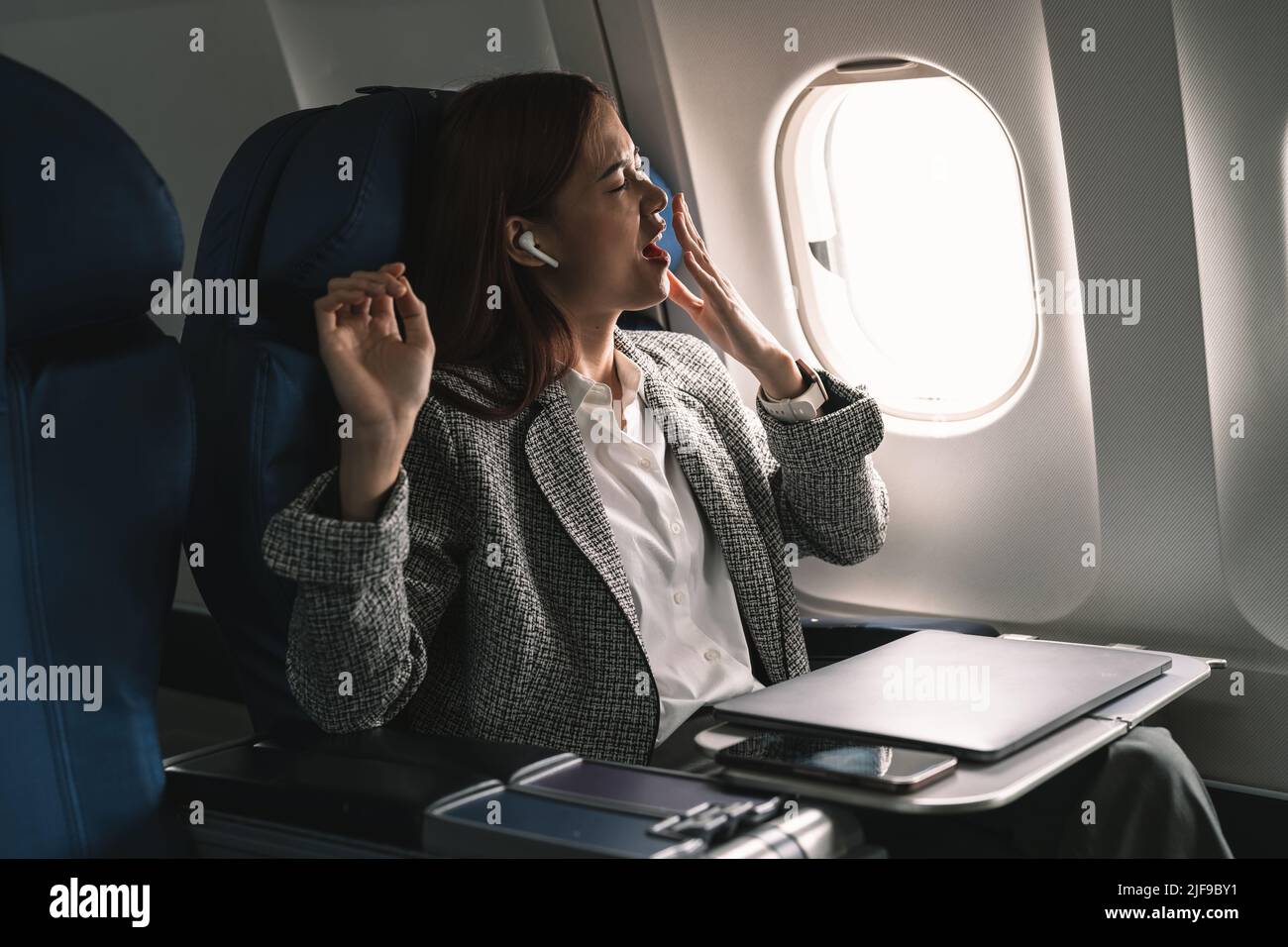 Sleepy and tired young asian businesswoman or female entrepreneur yawning feeling sleepy during a business flight to another city. Stock Photo