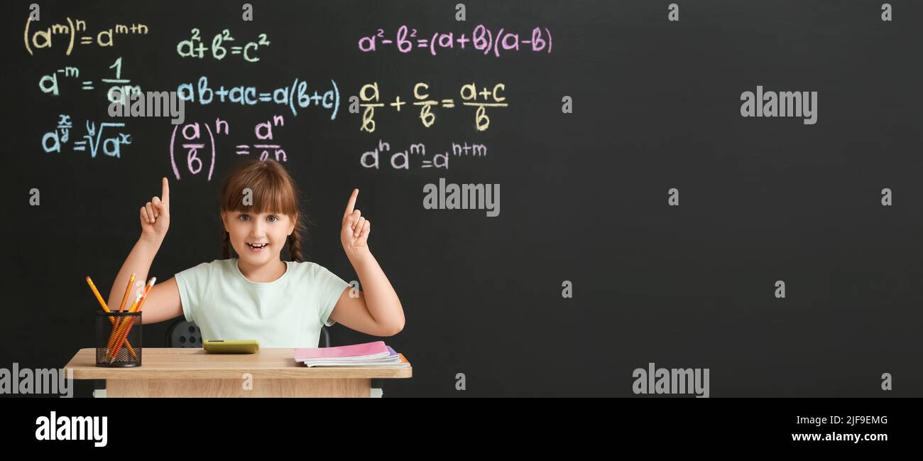 Cute schoolgirl sitting at desk during maths lesson in classroom Stock Photo