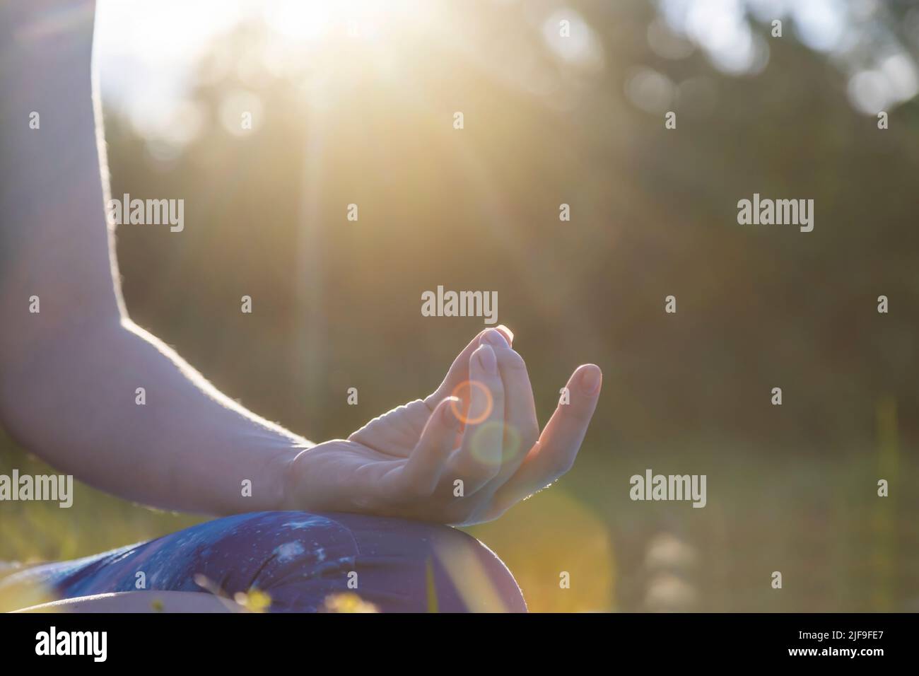 Woman in sportswear doing yoga, half lotus pose with mudra gesture, close-up. Wellness concept Stock Photo