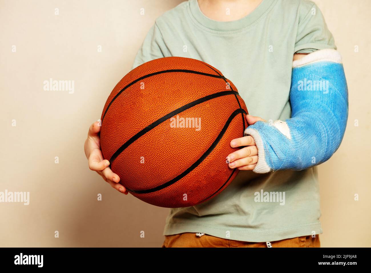 Big basketball ball in hands of boy with broken hand cast Stock Photo