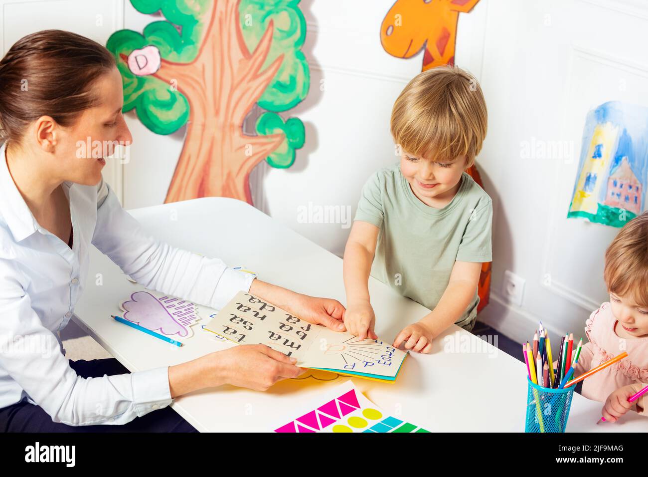 Woman teaches little kids to read letters in the book Stock Photo