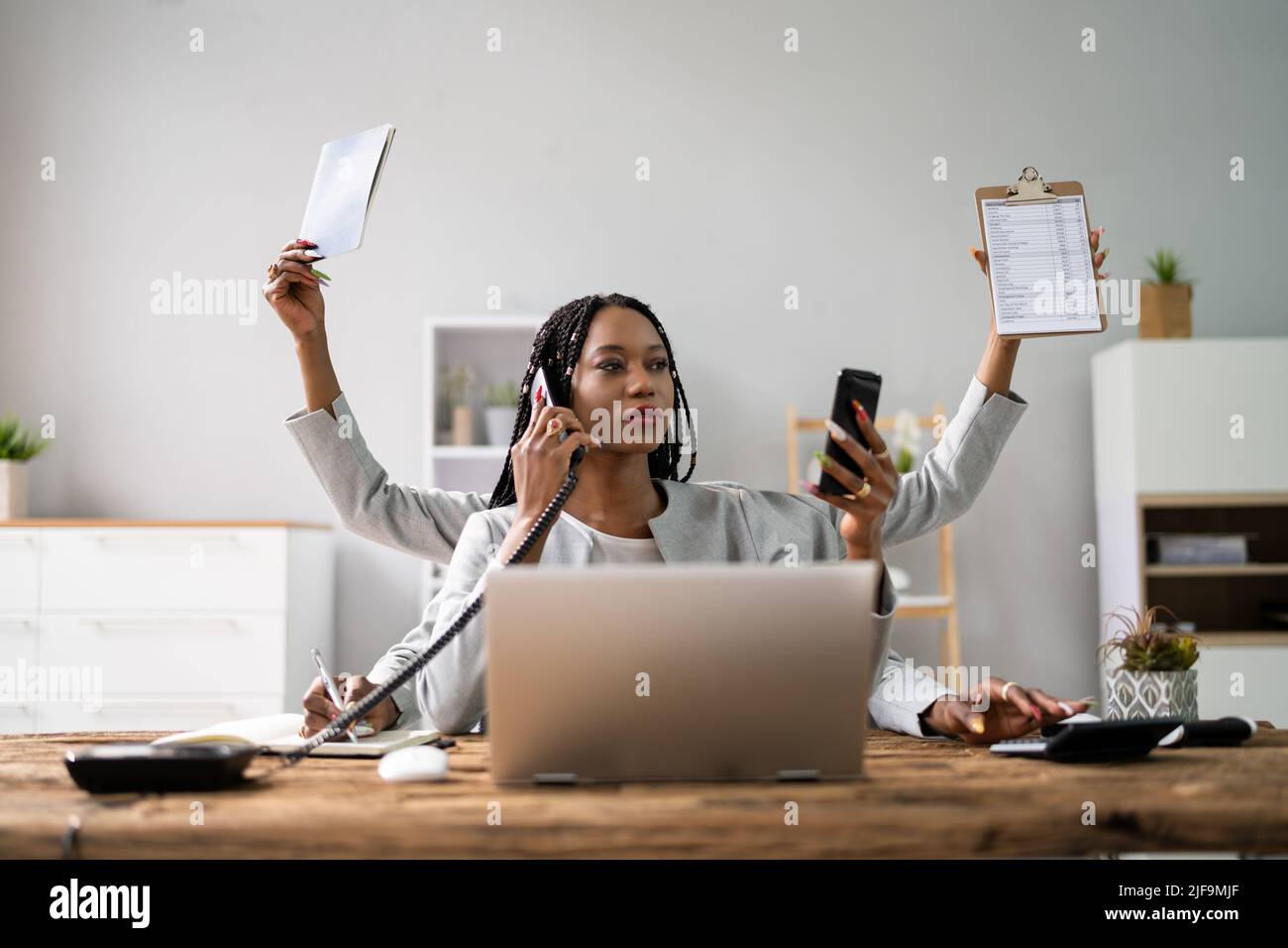 Smiling Young Businesswoman Doing Multitasking Work At Workplace Stock Photo