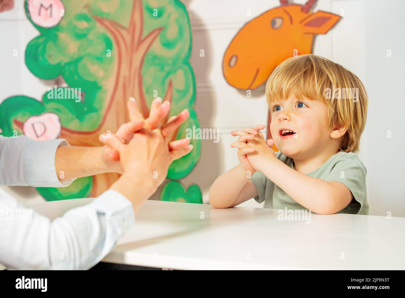 Cute blond boy play finger game sitting by the desk in class Stock Photo