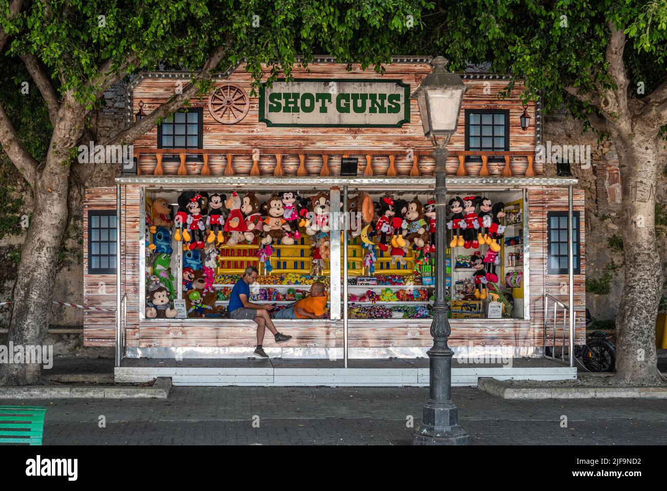 Two men talking in the shade at a colourful shooting gallery on a hot summer afternoon in Siracusa, Sicily, Italy Stock Photo