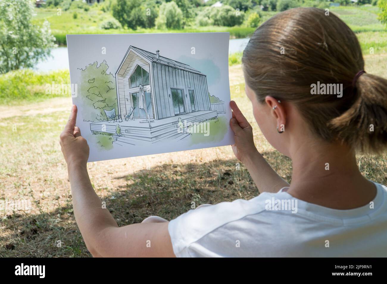 Architect holding barn house  hand drawn sketch in front of a plot of land.  Architectural design concept Stock Photo