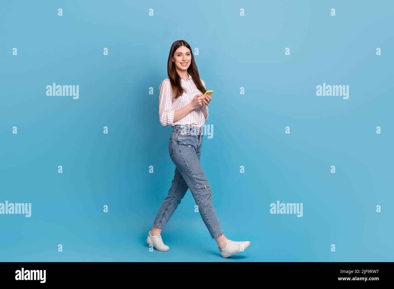 Full length body size view of attractive cheerful trendy girl using gadget strolling isolated over bright blue color background Stock Photo