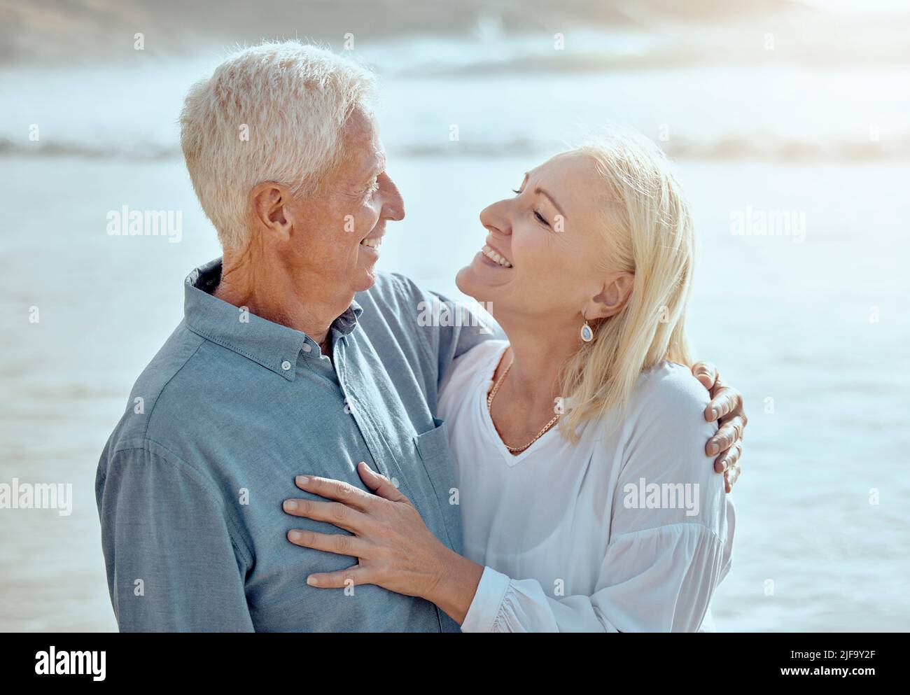 A happy mature caucasian couple enjoying fresh air on vacation at the beach. Smiling retired couple hugging and embracing while bonding outside Stock Photo