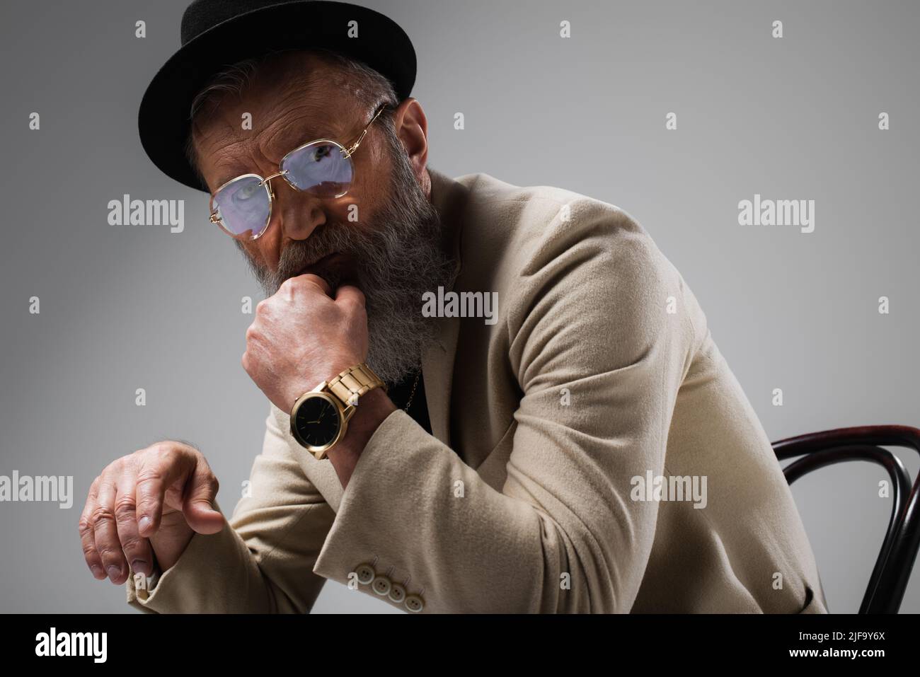 portrait of bearded senior man in stylish beige jacket and derby hat looking at camera on grey Stock Photo Alamy