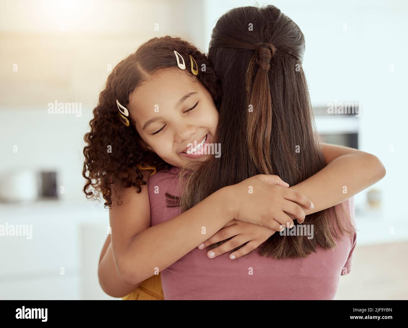 Mixed race single mother and daughter hugging in living room at home. Smiling hispanic girl embracing single parent and bonding in lounge. Happy Stock Photo