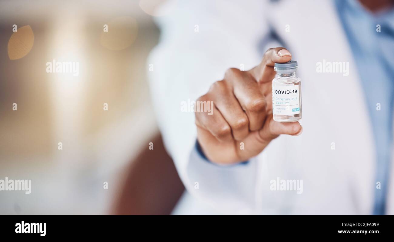 Closeup hand of african american woman doctor holding a bottle of the corona virus vaccine while standing in her hospital office. Be safe during the Stock Photo