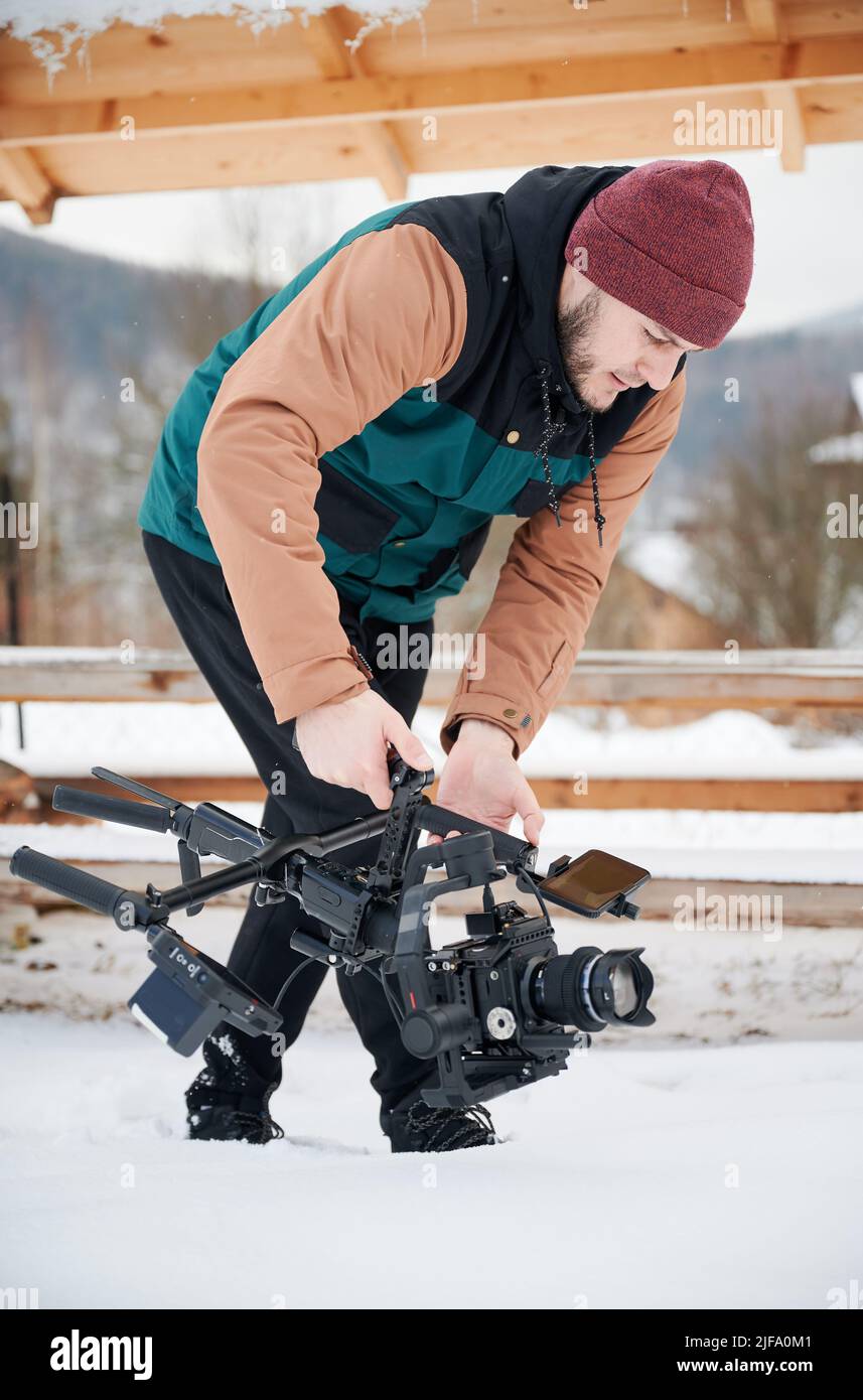 Videographer man walking on snow, shooting footage, using camera mounted on gimbal stabilizer equipment in winter. Stock Photo