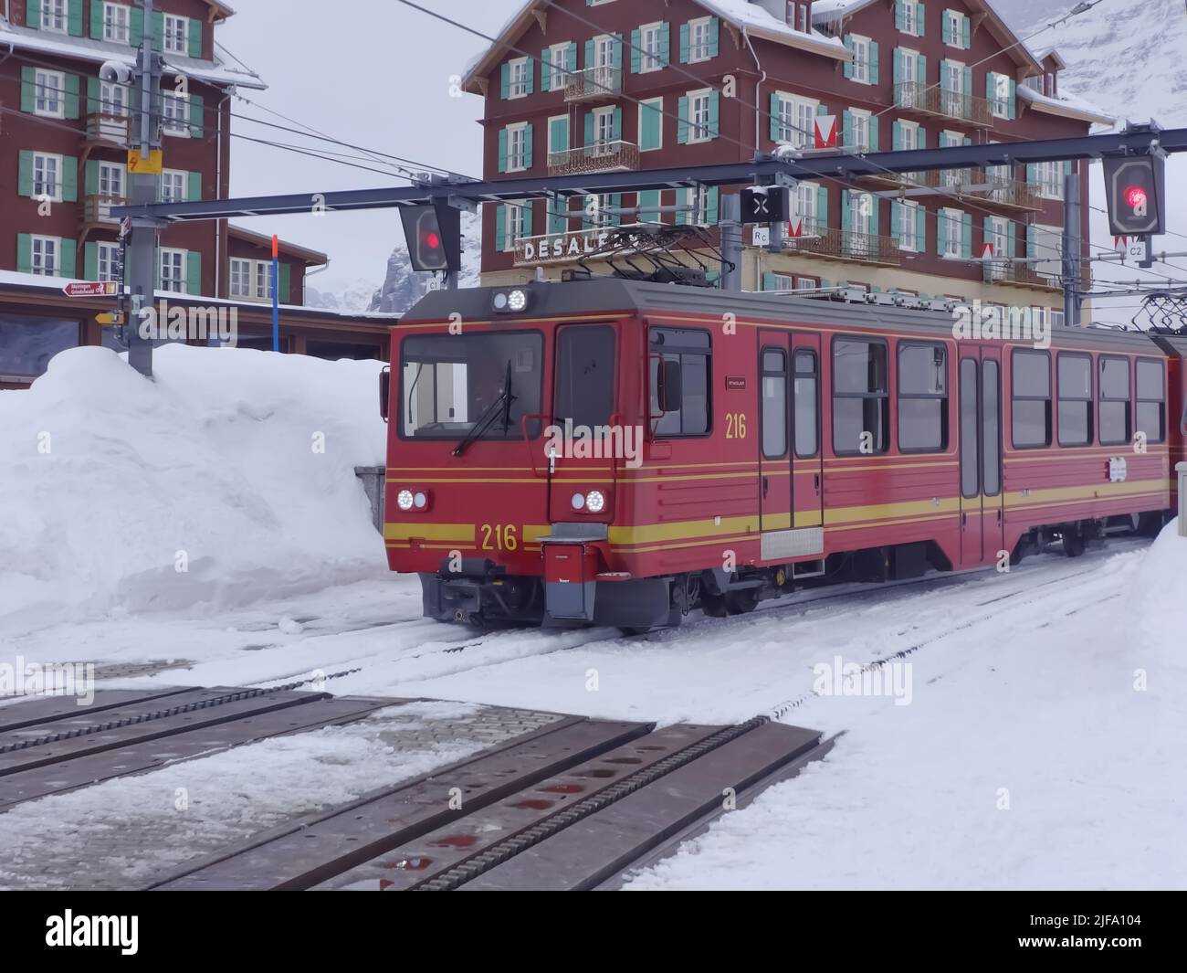 A view of a Train moving against Snow in Jungfrau in Switzerland with Hotels in Background and railway Signal Seen. They use Strub rack Railway trac Stock Photo