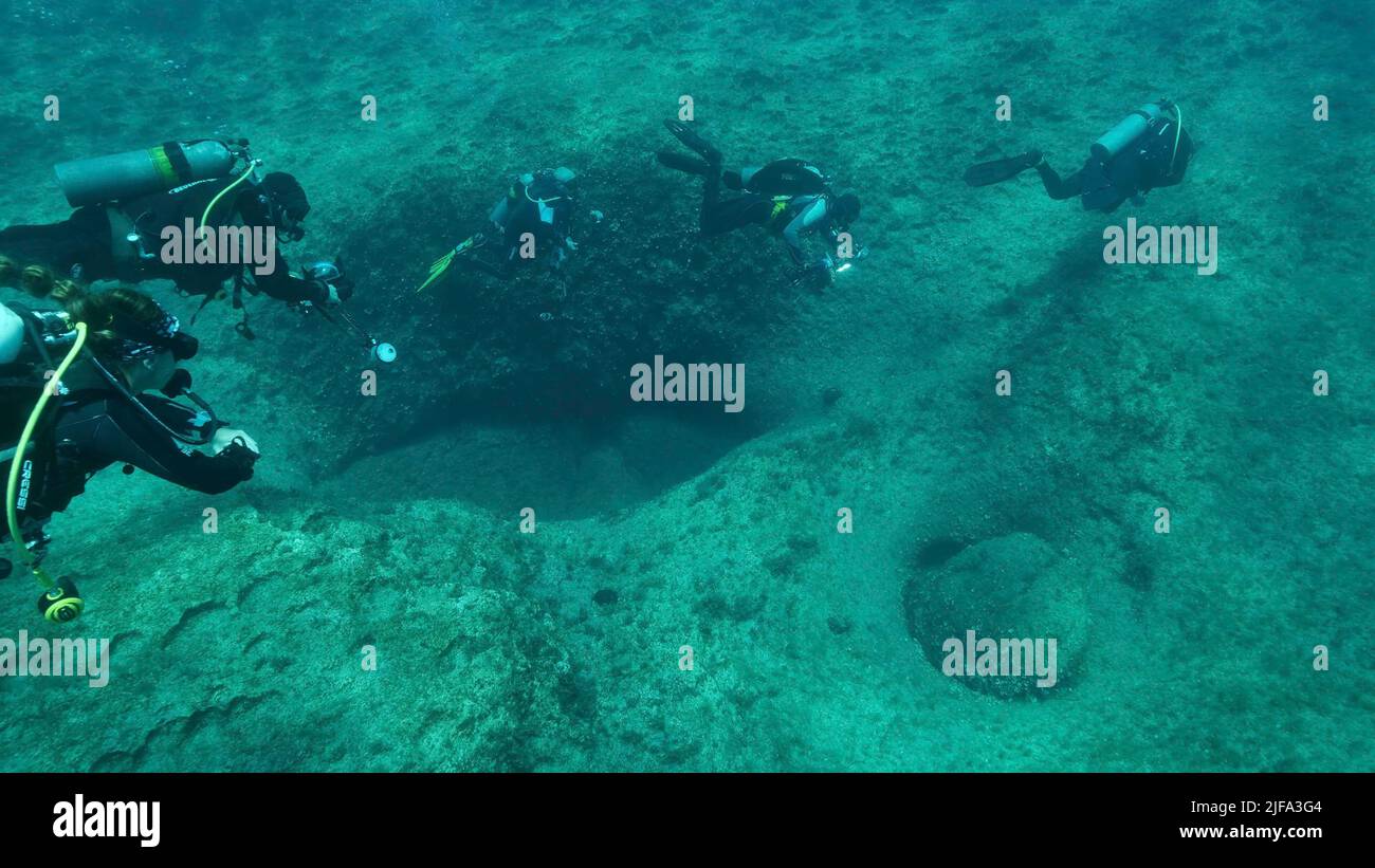 Group of scuba divers swims in the blue water above rocky seabed. Mediterranean Sea, Cyprus Stock Photo